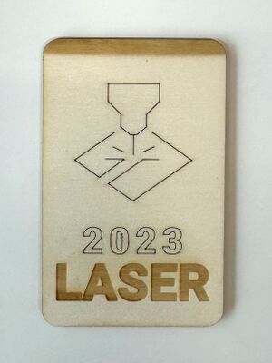 Laser-cut and engraved piece of ply based on example artwork. The ply is rectangular with rounded corners, with a shaded gradient at the top. It has an engraved line drawing of a laser beam, with the words "2023 LASER" engraved below.